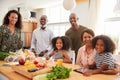 Portrait Of Grandparents Sitting At Table With Grandchildren Playing Games As Family Prepares Meal