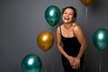 Portrait on gray background with copy space of beautiful woman in evening black dress posing against gold and green air balloons, Royalty Free Stock Photo