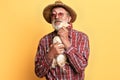 Gray-haired male farmer in straw hat, hugs with love his hen