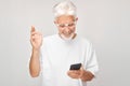 Portrait of gray-haired man in white T-shirt holding mobile phone in hand with happy smiling face. Person with smartphone Royalty Free Stock Photo
