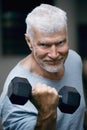 Portrait of a gray haired senior man with a dumbbell in his hand. Sport and health care concept