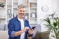 Portrait of a gray-haired senior man sitting at home on the sofa and using the phone. Smiling looking at the camera Royalty Free Stock Photo