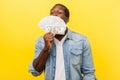 Portrait of greedy young man smelling dollar bills with pleased satisfied expression. indoor studio shot isolated on yellow