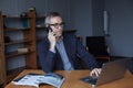 Portrait of grey hair elderly man sitting front table with laptop, talking on mobile phone Royalty Free Stock Photo