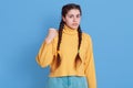 Portrait of grimacing sad girl model with pigtails, holding clasp hands in fists, wearing yellow jumper and jeans, posing isolated Royalty Free Stock Photo