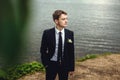 Portrait of the groom in nature in the summer. A handsome man in a suit stands on the shore of the pond and looks into the Royalty Free Stock Photo