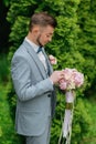 Portrait of the groom standing against the background of green trees and holding a wedding bouquet Royalty Free Stock Photo