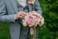 Portrait of the groom standing against the background of green trees and holding a wedding bouquet Royalty Free Stock Photo