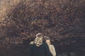 Portrait of the groom, standing with his back, the bride hugging him holding flowers, looking at the camera