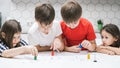 Portrait of group of busy children playing tabletop game, moving figures on white board with numbers, tracks, thinking.