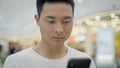 Portrait of hamdsome asian man scrolling phone on big mall background