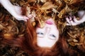 Portrait and hands of a natural young lady, covered with red and orange autumnal leaves. Beautiful woman lying