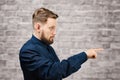 Portrait of handsome adult man on brick wall background. Caucasian man with beard showing finger aside Royalty Free Stock Photo