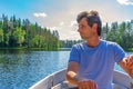 Portrait of handsome adult man holding oars in hands and floating on boat on northern lake. Happy vacationer sitting in boat