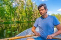 Portrait of handsome adult man holding oars in hands and floating on boat on northern lake. Happy vacationer sitting in boat