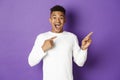 Portrait of handsome african-american guy in white sweatshirt, pointing fingers at upper right corner and smiling amazed Royalty Free Stock Photo