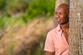 Portrait handsome African American man posing from behind a tree in the park. Man is smiling and glancing off camera Royalty Free Stock Photo