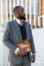 Portrait of handsome afro american businessman using phone in suit against modern building exterior. reflection in glass Royalty Free Stock Photo