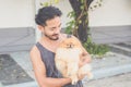 Portrait of a handsome Asian man with short hair wearing a dark gray tank top and blue jeans. Hold his Pomeranian and play with it Royalty Free Stock Photo