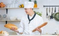 Portrait handsome Asian professional male chef wearing white uniform, hat, showing, holding baguette, bread, cooking breakfast in Royalty Free Stock Photo