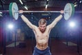 Portrait of a handsome athlete . Athlete raises the barbell over your head. shots in the dark tone. Cross fit style Royalty Free Stock Photo