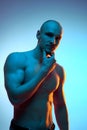 Portrait of handsome, bald, muscular young man standing with shirtless relief body, posing against blue studio Royalty Free Stock Photo
