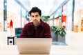 Portrait of handsome bearded freelancer male sitting at table in shopping mall working on laptop, looking at camera. Royalty Free Stock Photo