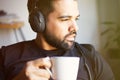Portrait of handsome bearded man in headphones listening to music at home and drinking coffee. Relaxing and rest time Royalty Free Stock Photo