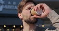 Portrait of handsome bearded man holding cup of take-out coffee and smiling standing on street on nice day, drinking Royalty Free Stock Photo