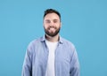 Portrait of handsome bearded young man in casual outfit smiling and looking at camera over blue studio background Royalty Free Stock Photo