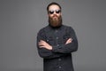 Portrait of handsome bearded young man with serious expression wearing sunglasses with crossed hands over gray background Royalty Free Stock Photo