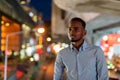 Portrait of handsome black African businessman outdoors in city at night smiling and thinking Royalty Free Stock Photo