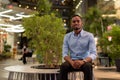 Portrait of handsome black African businessman sitting outdoors in city at night while smiling Royalty Free Stock Photo