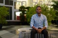 Portrait of handsome black African businessman sitting outdoors in city at night while smiling Royalty Free Stock Photo