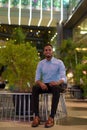 Portrait of handsome black African businessman sitting outdoors in city at night while smiling Royalty Free Stock Photo