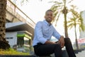Portrait of handsome black African businessman sitting outdoors in city during summer while smiling Royalty Free Stock Photo