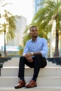 Portrait of handsome black African businessman sitting outdoors in city during summer Royalty Free Stock Photo