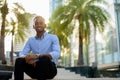 Portrait of handsome black African businessman sitting outdoors in city during summer Royalty Free Stock Photo