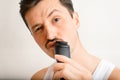 Portrait of handsome brutal young man shaving with modern electric razor and looking at camera. Selective focus on trimmer Royalty Free Stock Photo