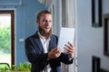 Portrait handsome businessman with beard holding tablet standing at side window office. happy smart man mature wear suit Royalty Free Stock Photo