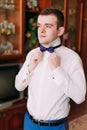 Portrait of handsome businessman in blue suit putting on bow-tie indoors Royalty Free Stock Photo