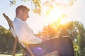 Portrait of handsome businessman drinking coffee and reading newspaper while sitting on folding chair in park Royalty Free Stock Photo