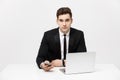 Portrait of a handsome businessman holding smartphone while working on a computer at his desk. He is in a office his Royalty Free Stock Photo