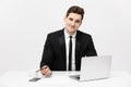 Portrait of a handsome businessman holding smartphone while working on a computer at his desk. He is in a office his Royalty Free Stock Photo