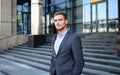 Portrait of a handsome businessman in a suit standing outside a city building.