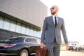 Portrait of a handsome businessman in sunglasses standing near the car outdoors in front of the modern building facade Royalty Free Stock Photo