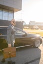 Portrait of a handsome businessman in sunglasses standing near the car outdoors in front of the modern building facade Royalty Free Stock Photo