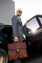 Portrait of a handsome businessman in sunglasses standing near the car outdoors in front of the modern building facade Royalty Free Stock Photo