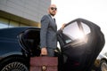 Portrait of a handsome businessman in sunglasses standing near the car outdoors in front of the modern building facade Royalty Free Stock Photo