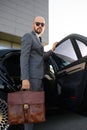 Portrait of a handsome businessman in sunglasses standing near the car outdoors in front of the modern building facade Royalty Free Stock Photo